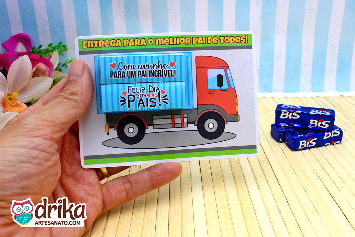 Cartão de Dia dos Pais com design de caminhão vermelho porta bis sendo segurado por uma mão.